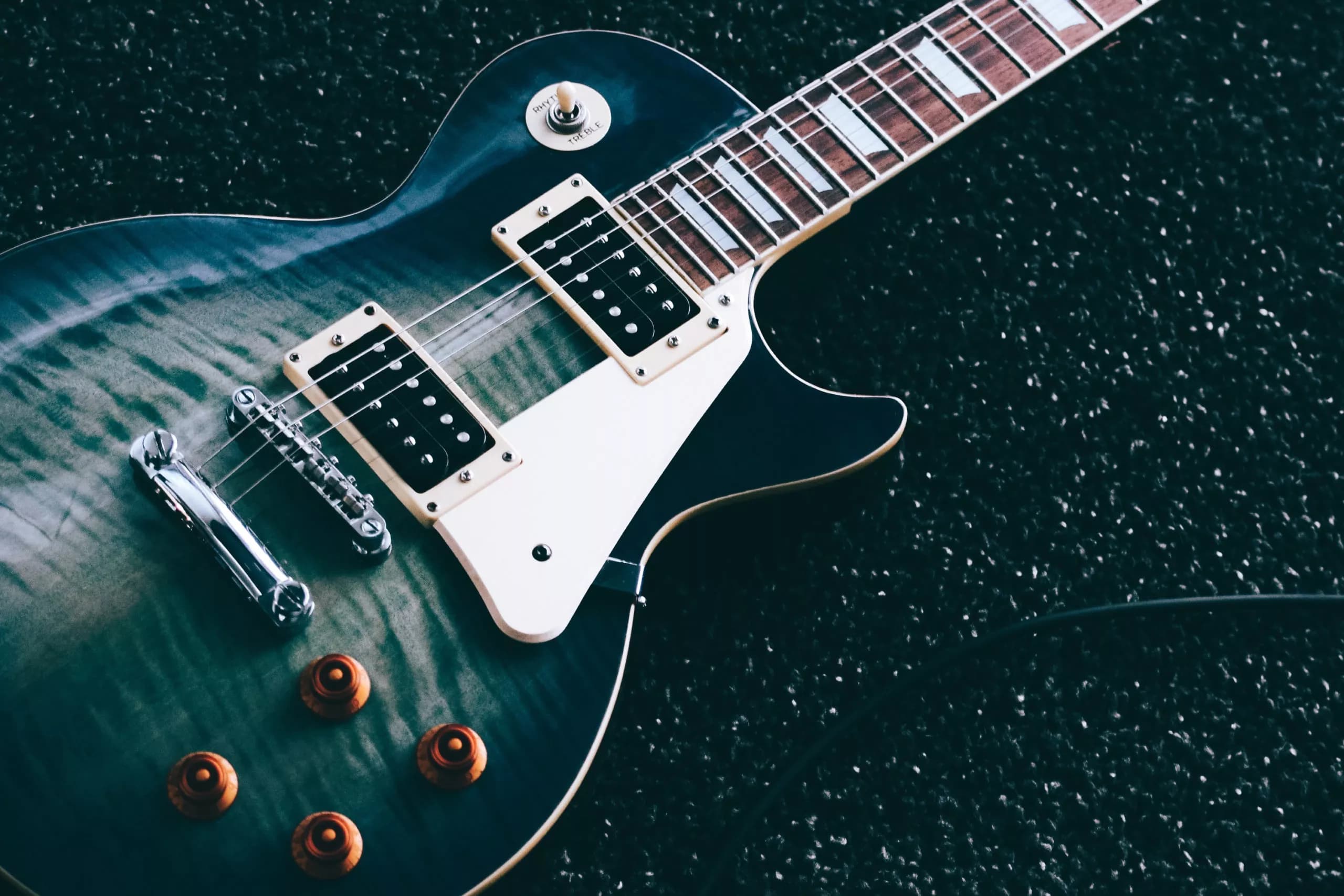 Blue flame-top Gibson Les Paul electric guitar resting on a dark speckled surface